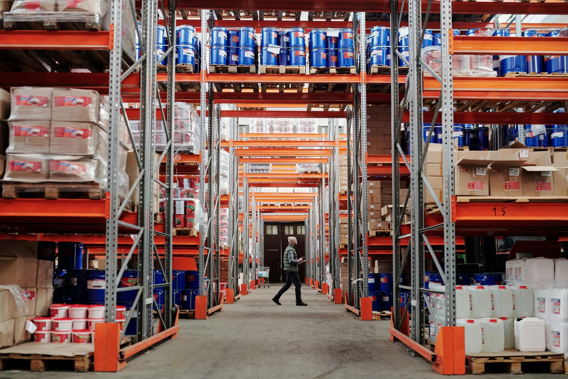Warehouse worker walking between tall industrial storage racks filled with boxes