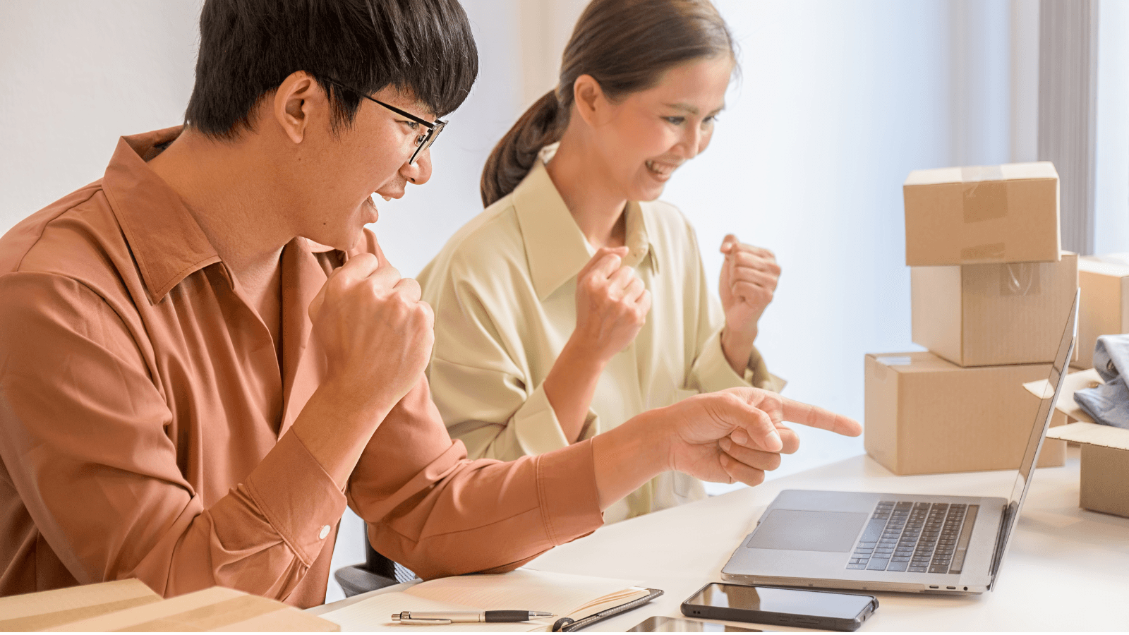 Two ecommerce business owners celebrating successful order fulfillment using a multi-channel system on a laptop
